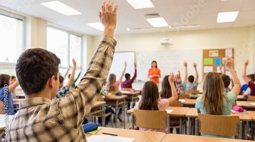 Male student raising hand to answer question in a busy high school class