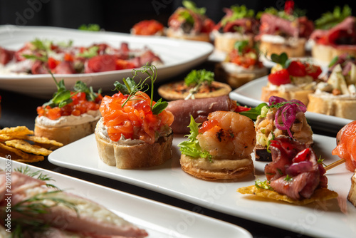 Fotografie A selection of gourmet catering appetizers and canapes with salmon, shrimp, prosciutto, and caviar on white plates, perfect for a party buffet or holiday celebration