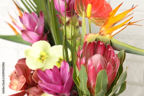 Bouquet of beautiful tropical flowers near white brick wall, closeup