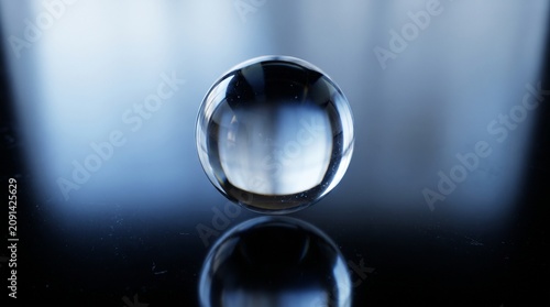 Polished glass sphere sitting on a dark reflective surface captures soft blue ambient light in this sharp macro photography shot