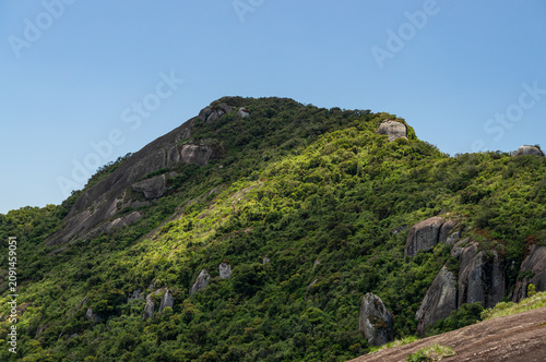 Granite cliffs and lush Atlantic forest green vegetation slopes under clear sky highlighting wild terrain under summer morning sunny clear blue sky in Monte Verde, Camanducaia, Minas Gerais, Brazil.