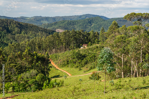 Panoramic view of rolling green hills, forested valleys and mountains under dramatic summer afternoon clouded sky inside Fazenda Off Road in Monte Verde, Camanducaia, Minas Gerais - Brazil.