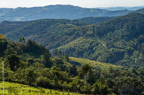 Panoramic view of forested hills and layered valleys under soft summer afternoon light and blue sky saw from Fazenda Off Road farm in Monte Verde, Camanducaia, Minas Gerais - Brazil.