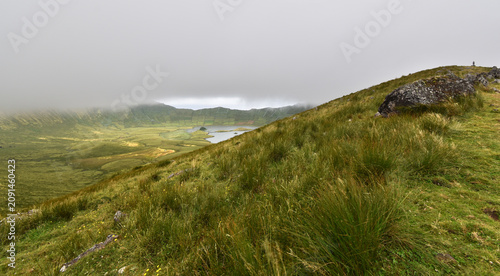 Canvastavla A breathtaking panoramic view of the caldera with its tranquil lakes, surrounded by lush green terraced slopes and dramatic rock formations under a cloudy sky, Corvo Island, Azores