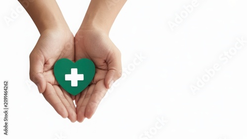 Hands holding a green heart with a white cross, isolated on white background