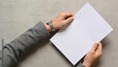 Top view of professional hands in a suit holding a blank white paper on a gray background mockup
