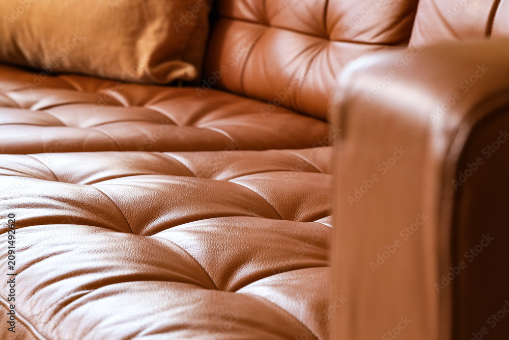 Obraz premium Brown leather sofa with tufted cushions and a soft pillow, comfortable home furniture detail, this furniture piece offers a warm and inviting atmosphere