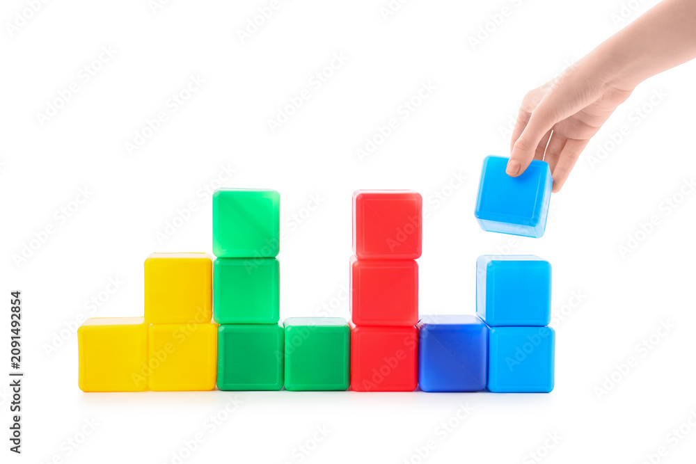 Obraz premium Hand placing a blue building block on a stack of colorful toy cubes, growth and development
