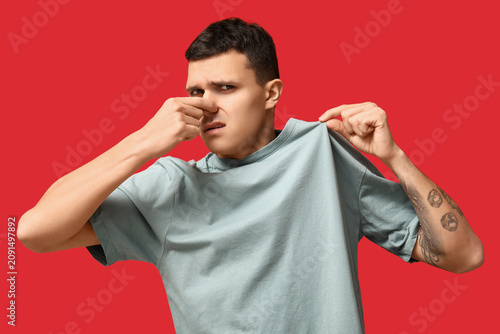 Cuadro en lienzo Handsome young man feeling bad smell from dirty clothes on red background
