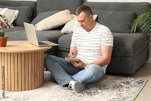 Mature male freelancer writing in notebook at home