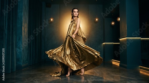Elegant Woman in Flowing Golden Dress Posing in Modern Interior
