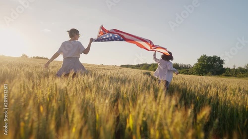 Mother and young son run through wheat field carrying United States flag during sunset. Golden hour, family values and patriotic spirit symbolize freedom, national pride and American heritage.