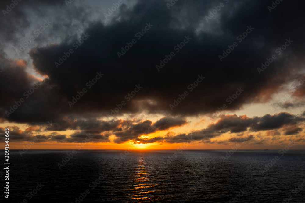Fototapeta premium Dramatic sunset over the dark ocean with heavy clouds and golden light reflection