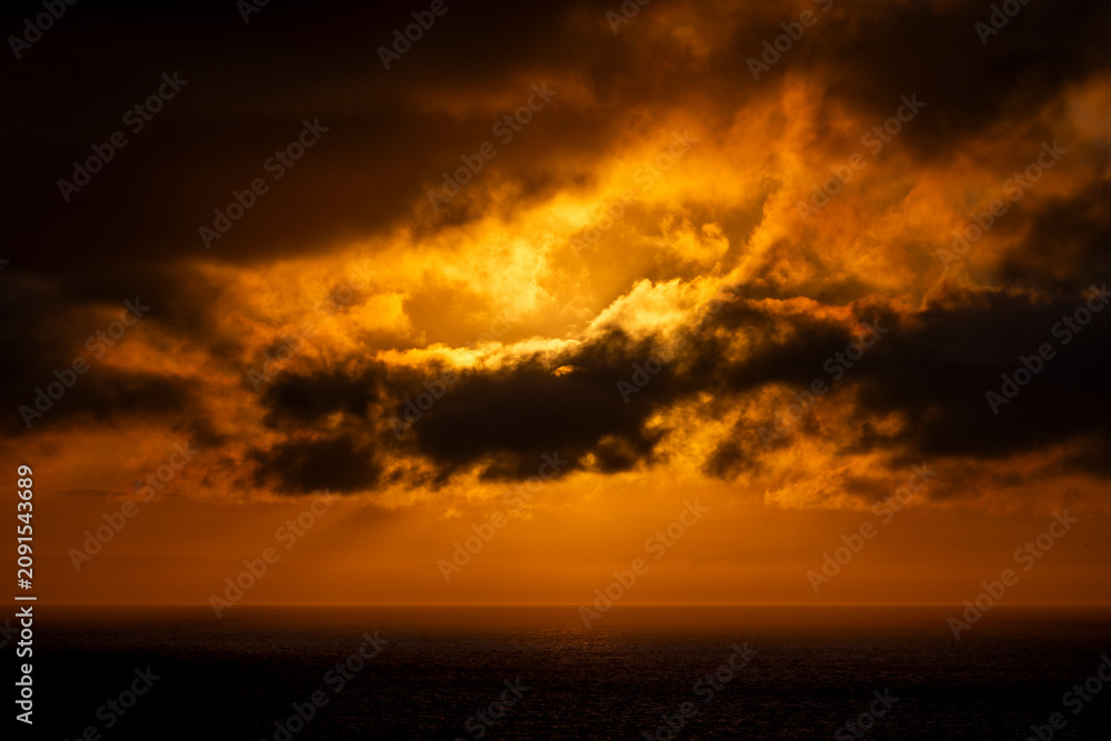 Fototapeta premium Dramatic sunset clouds over the ocean with golden light rays breaking through