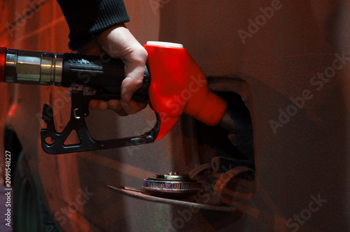 Night street city photo. Man fills car with gasoline. Male hand holds red petrol gun, fuel dispenser, petroleum dispensing nozzle on gas station. Concept of crisis in Russia, rising oil prices, sale