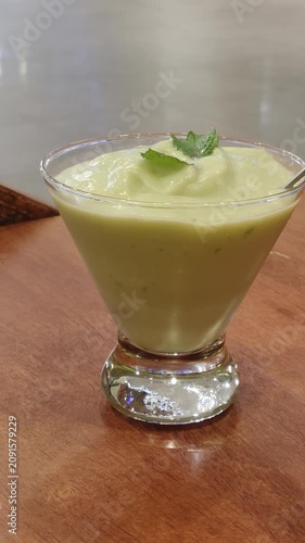 A creamy avocado ice blended drink served in a clear glass, topped with fresh mint leaves, offering a refreshing and healthy beverage perfect for warm weather.