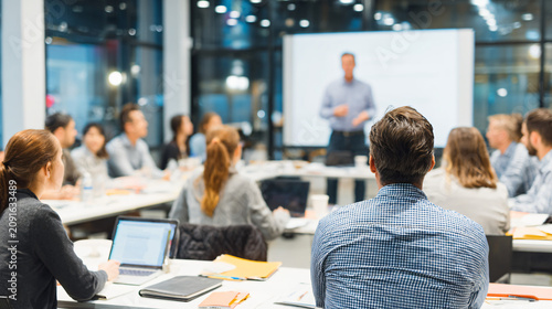 Corporate training session in a modern office classroom, instructor explaining strategy to employees seated with notebooks and laptops