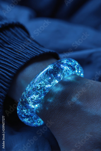Glowing transparent blue bracelet with sparkling light effects worn on wrist, creating magical and futuristic appearance in low light