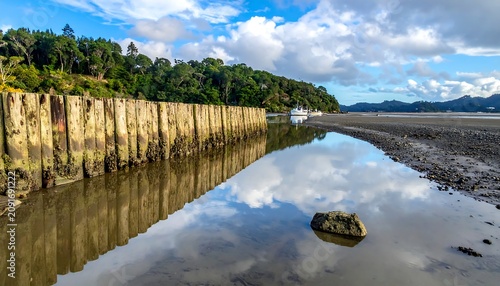 Calm Tidal Inlet Reflecting Cloudy Blue Sky Beside Wooden Seawall and Forested Shore
