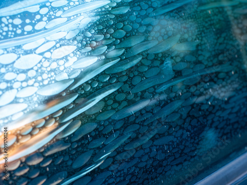 Air bubbles trapped in old deteriorated car window tint film, damaged adhesive layer on glass surface with peeling texture, vehicle maintenance problem and poor installation concept