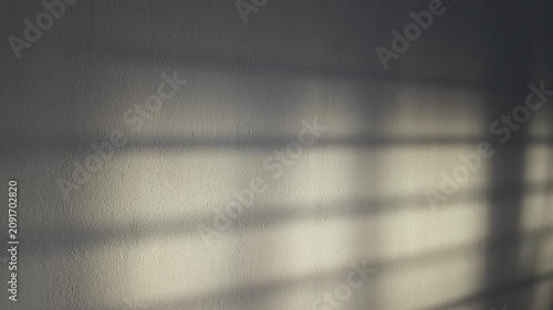Soft natural sunlight casts gentle window-frame shadows across a textured interior wall, creating a calm, minimalist atmosphere with warm tones and abstract geometric patterns.