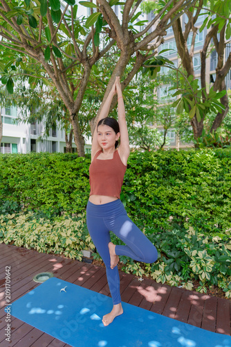 Asian Gen Z woman practicing standing yoga pose in urban park promoting wellness mindfulness and healthy lifestyle