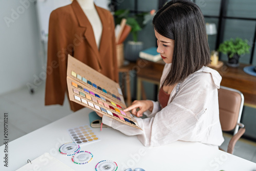 Asian woman designer selecting fabric samples while creating fashion collection in creative studio