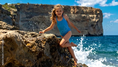A Young Girl Balances on Rocky Shore As Waves Crash Against Cliffs Under a Blue Sky