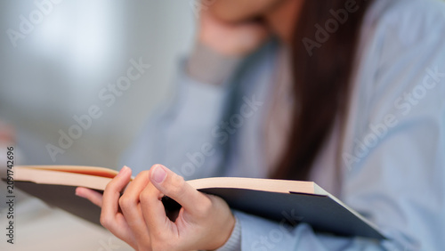 Adult woman holding open book while studying in blurred educational environment with copy space