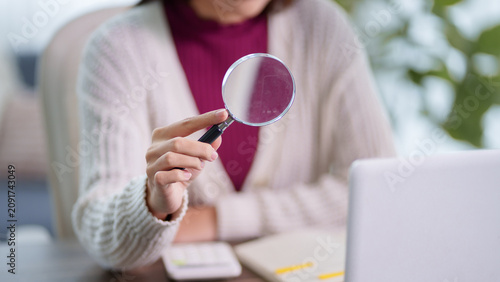 Fotografía Adult woman holding magnifying glass while studying or researching with laptop a