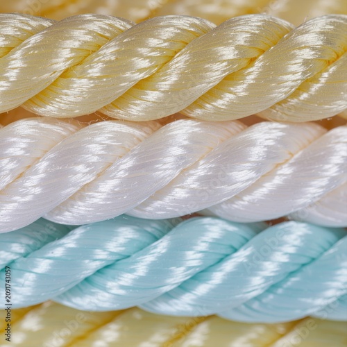 Close-up macro of three thick, braided synthetic ropes in pastel colors: cream, white, and pale blue.