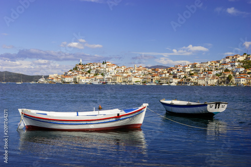 Konstfotografi Two boats float on the blue water in front of a hillside town with white buildings and red roofs under a blue sky with clouds