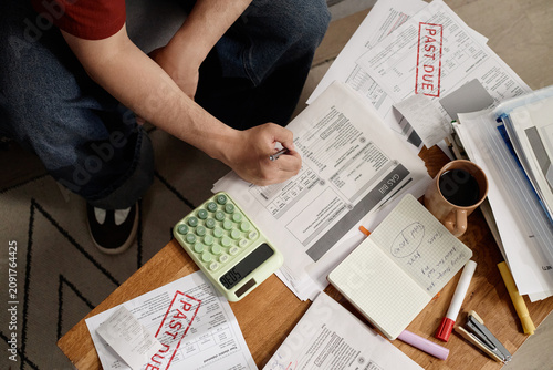 Quadro su tela Overhead shot of young adult man reviewing overdue utility bills, calculating expenses, managing household debt and budget stress