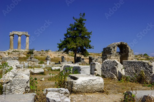Ancient ruins of the Temple of Apollo in Corinth, Greece, under a clear blue sky.