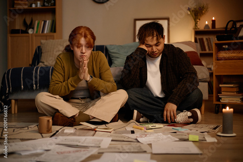 Cuadro en lienzo Young adult woman and Asian man sitting on floor, reviewing bills and paperwork, showing financial stress and household budgeting