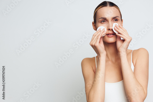 Cuadro en lienzo A woman uses cotton pads to wipe her face in a bright, minimal room, highlightin