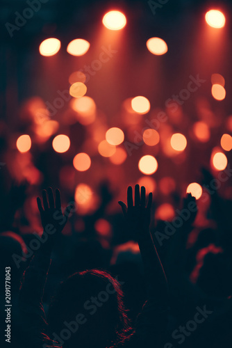 Raised hand in crowd at live music concert with colorful stage lights and blurred audience, festival atmosphere and entertainment event	