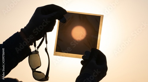 Hands holding sunglasses and a photo of the sun at sunrise