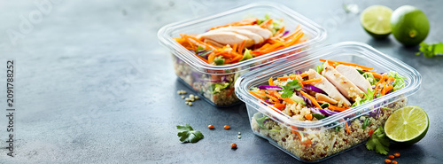 Two plastic meal prep containers with grilled chicken and fresh vegetables on a dark background with large copy space