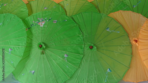 A vibrant collection of traditional paper umbrellas in various shades of green and yellow, creating a visually appealing display of handcrafted artistry and cultural heritage