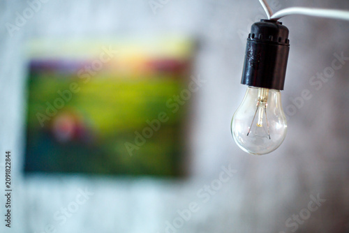 Fotografía Glowing Incandescent Light Bulb Hanging on a White Wire