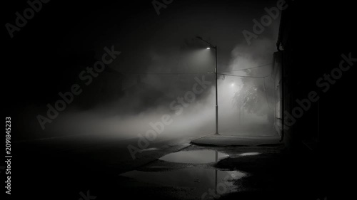 Foggy night street illuminated by lampposts with reflections in puddles creating eerie atmosphere