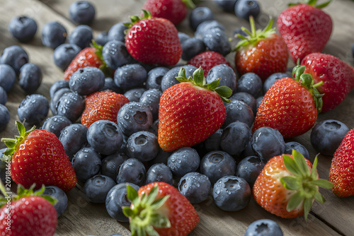 Fresh strawberries and blueberries scattered on a rustic wooden surface healthy summer fruit mix for food photography and healthy.