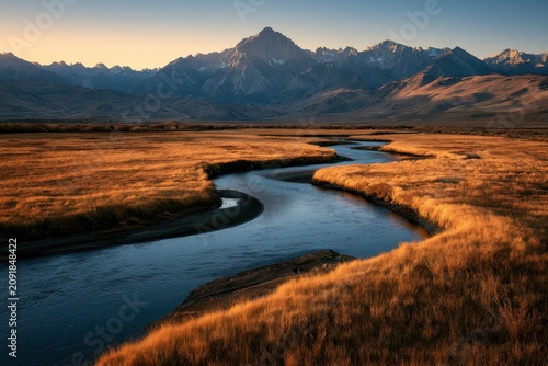 Winding river meandering through golden autumn meadows in a rugged mountain valley at sunset for outdoor travel and environmental branding