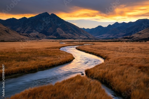 Sinuous river flowing through golden alpine meadows toward distant mountains at sunset in a wide-angle landscape for travel and tourism branding
