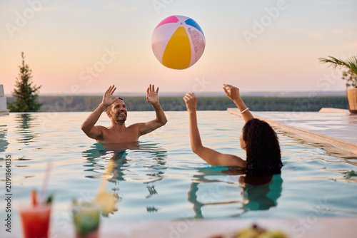 Playful couple having fun while playing volleyball in the pool.