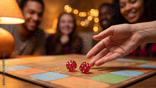 Board game night photo close up of red dice thrown on table with happy friends cheering behind