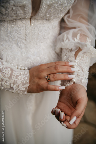 The bride in a white dress embroidered with various patterns and pearl details, buttons up her sleeve, showing off her manicure on her fingers