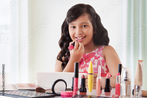 Cute girl putting on lipstick at home