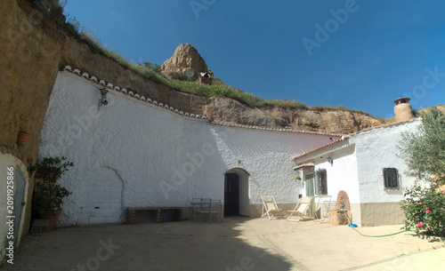 Traditional white troglodyte cave house facade with courtyard and chimneys carved in tuff rocks in Guadix, Spain
